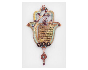 May include: A copper-toned Hamsa hand with a tree and two birds inside. The Hamsa is decorated with turquoise and purple beads. The Hamsa has a Hebrew inscription that reads "Berchat Habayit" which means "Blessing of the Home".
