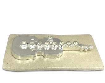 May include: A silver menorah shaped like a violin on a beige ceramic base.