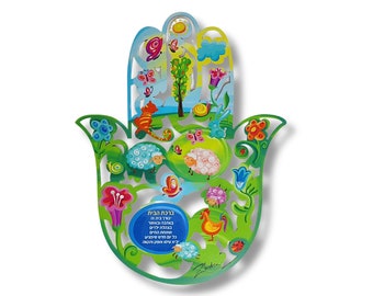 May include: A colorful Hamsa hand-shaped wall hanging with a green outline. The design features a blue sky, a tree, butterflies, sheep, flowers, and a blue oval with text. The artwork is vibrant and detailed, with a whimsical style.