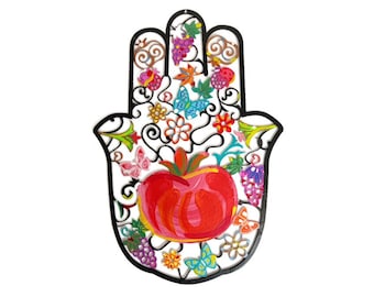 May include: A colorful metal hamsa hand wall decor with a red apple in the center. The hamsa is decorated with flowers, butterflies, and grapes.