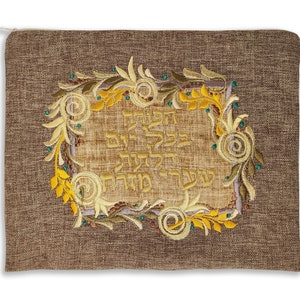 Puede incluir: Un chal de oraci&oacute;n de tela marr&oacute;n con un dise&ntilde;o bordado en oro que presenta texto hebreo y motivos florales.