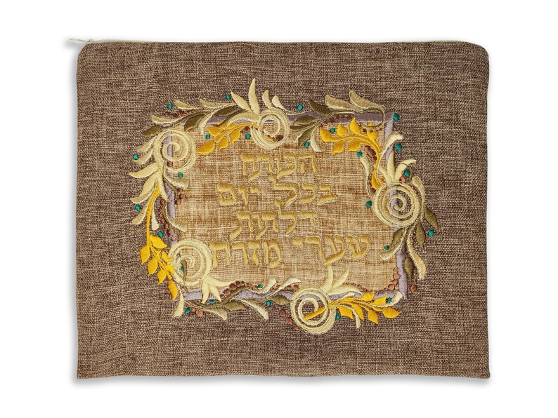 Puede incluir: Un chal de oraci&oacute;n de tela marr&oacute;n con un dise&ntilde;o bordado en oro que presenta texto hebreo y motivos florales.