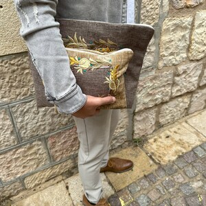 Puede incluir: Dos clutches de tela bordada, una marr&oacute;n con un dise&ntilde;o floral y otra beige con un dise&ntilde;o similar. Las clutches se sostienen en la mano de una persona.