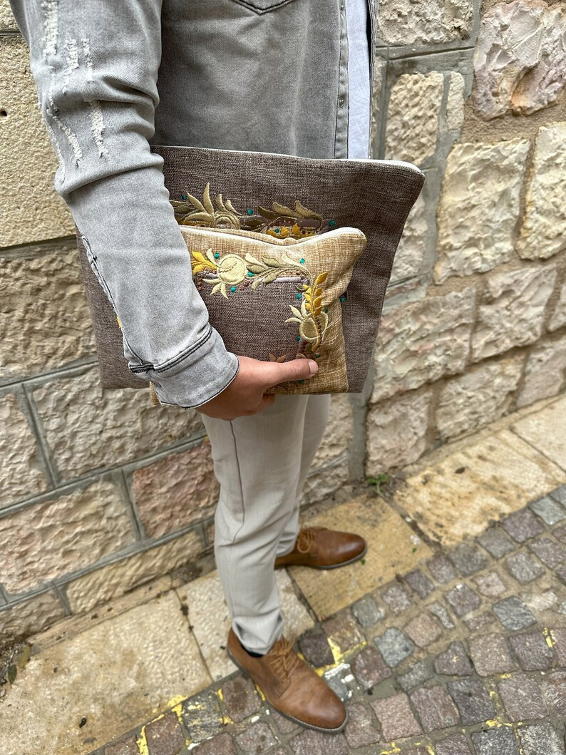 Puede incluir: Dos clutches de tela bordada, una marr&oacute;n con un dise&ntilde;o floral y otra beige con un dise&ntilde;o similar. Las clutches se sostienen en la mano de una persona.