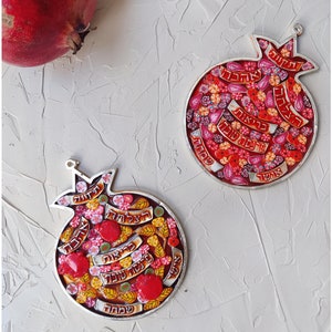 K&ouml;nnte beinhalten: Zwei silberne Granatapfel-Ornamente mit roten, gelben und wei&szlig;en Mosaikmustern. Die Ornamente zeigen hebr&auml;ischen Text und sind ein traditionelles Symbol von Rosh Hashanah.