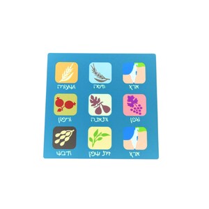 Può includere: Un gioco da tavolo quadrato blu con nove quadrati illustrati e testo ebraico. Le immagini raffigurano grano, fichi, uva e altri simboli agricoli. Il gioco è progettato per uso educativo o ricreativo.