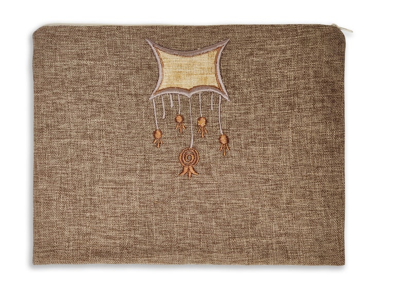 Puede incluir: Una bolsa de tela marr&oacute;n con cremallera y un dise&ntilde;o bordado beige y marr&oacute;n de una forma geom&eacute;trica con borlas colgantes.