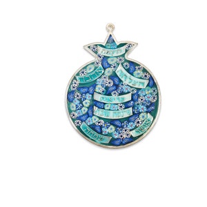 K&ouml;nnte beinhalten: Ein silberner und blauer Wandbehang in Form eines Granatapfels mit hebr&auml;ischem Text und floralen Designs. Der Text lautet "Shalom", "Ahava", "Simcha", "Derech", "Tzedakah", "Emet", "Chesed", "Shalom" und "Tzedek".