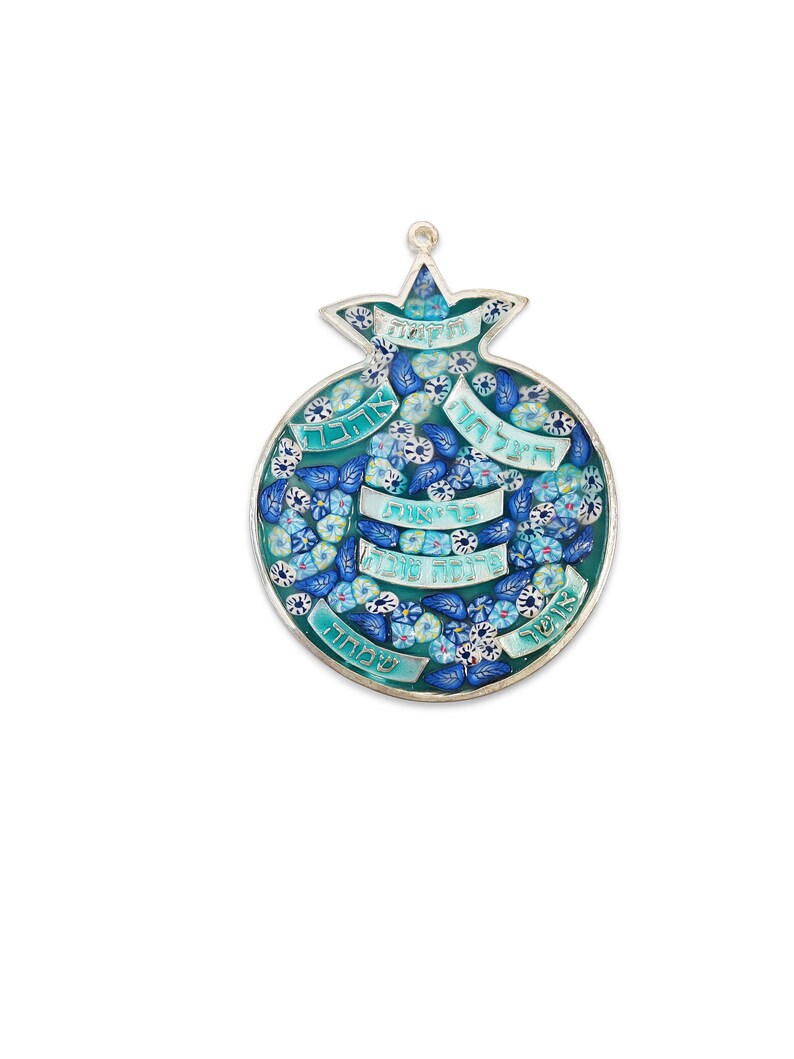 K&ouml;nnte beinhalten: Ein silberner und blauer Wandbehang in Form eines Granatapfels mit hebr&auml;ischem Text und floralen Designs. Der Text lautet "Shalom", "Ahava", "Simcha", "Derech", "Tzedakah", "Emet", "Chesed", "Shalom" und "Tzedek".