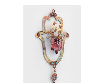 May include: A copper-toned Hamsa hand wall hanging with a pomegranate and two birds. The Hamsa is decorated with turquoise beads and a dangling spiral charm.