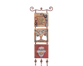 May include: A three-piece wall hanging with a copper finish. The top piece features a home blessing in Hebrew and English. The middle piece features a tree of life design. The bottom piece features a Hamsa hand with a turquoise eye. The hanging is adorned with copper beads.