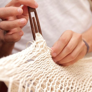 close up of an mans hands handweaving a cotton hammock