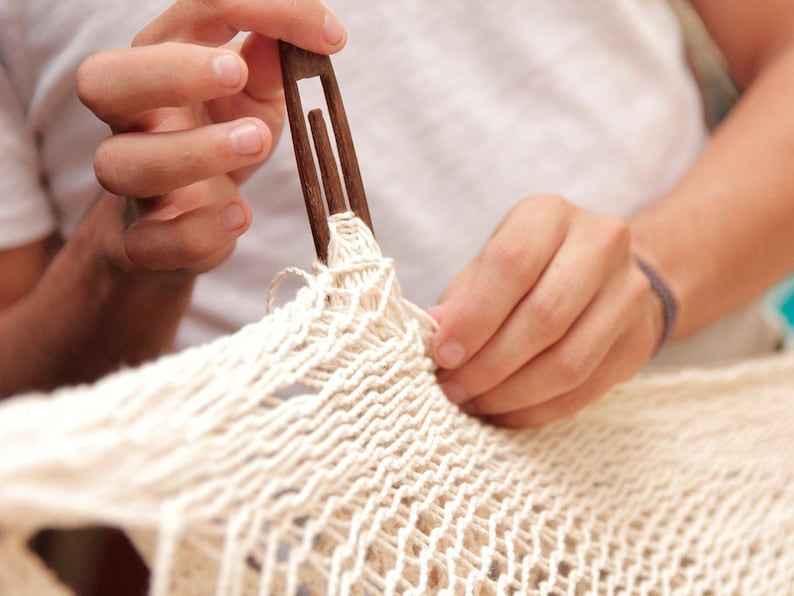 close up of an mans hands handweaving a cotton hammock