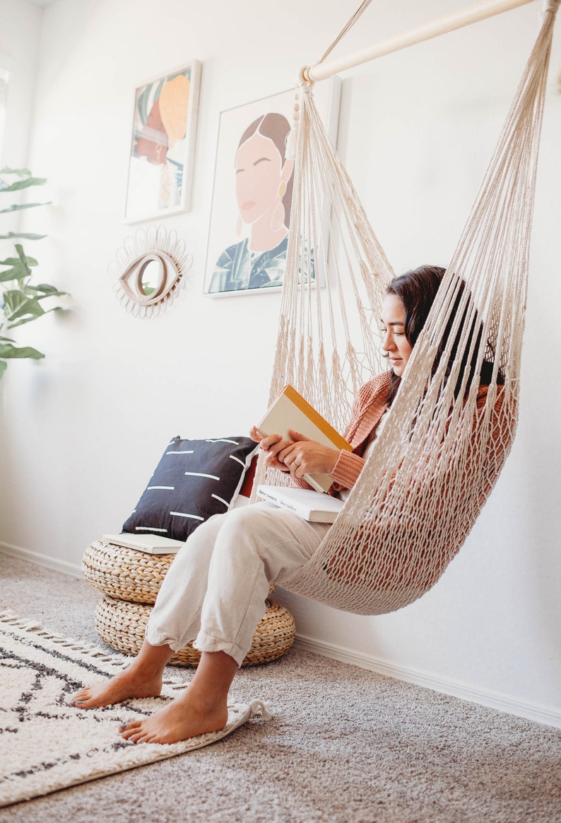 woman sitting on an indoor swing chair and reading a book