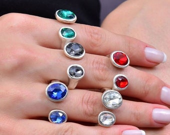 May include: A set of silver rings with colorful gemstones. The rings feature a variety of colors, including blue, green, red, and clear. The rings are all set with round gemstones.