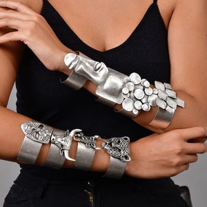 Puede incluir: Cuatro pulseras de plata con diferentes diseños. Las pulseras presentan una cara humana, una cabeza de toro, un jaguar y un grupo de círculos.