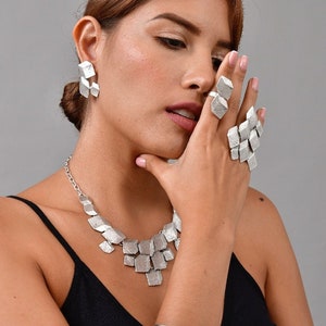 Peut inclure: Une femme portant un collier, des boucles d'oreilles, une bague et un bracelet en argent. Les bijoux sont faits de formes géométriques.