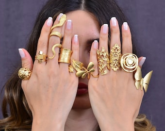 May include: A woman's hands wearing a variety of gold rings, including a snake ring, a butterfly ring, and a floral ring.