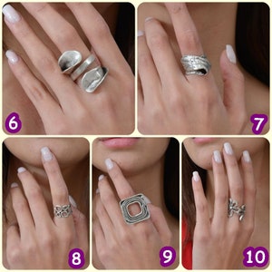 May include: Five different silver rings on a hand. The rings are all unique in design and style.