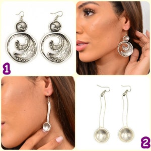 May include: Two pairs of silver earrings. The first pair features a round design with a wave pattern. The second pair is long and features a round pendant at the bottom.