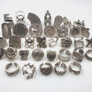 Peut inclure: Une collection de 30 bagues argentées avec différents motifs, y compris des formes géométriques, des fleurs et des motifs abstraits.