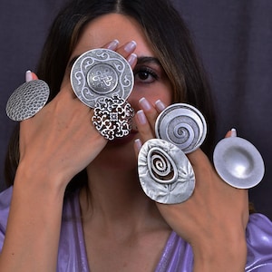 Può includere: Cinque anelli d'argento con diversi design. Gli anelli sono indossati sulle dita di una persona. Gli anelli sono tutti in metallo e hanno una finitura lucida.