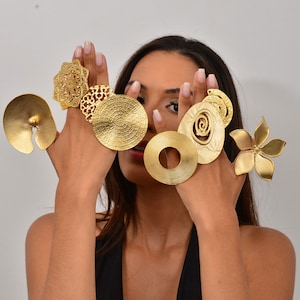 Könnte beinhalten: Eine Frau trägt verschiedene goldene Ringe an ihren Fingern. Die Ringe sind alle in verschiedenen Formen und Größen, einige haben komplizierte Designs. Die Ringe sind aus glänzendem Gold gefertigt.