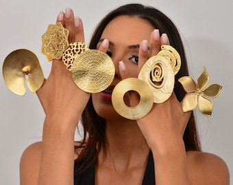 May include: A woman is wearing a variety of gold rings on her fingers. The rings are all different shapes and sizes, and some have intricate designs. The rings are made of a shiny gold metal.