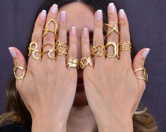 May include: A woman's hands wearing a variety of gold rings with unique and intricate designs. The rings are stacked on each finger, creating a bold and stylish look.