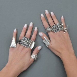 May include: A pair of hands wearing a variety of silver rings. The rings are all different shapes and sizes, and some have intricate designs. The rings are worn on the index, middle, and ring fingers of both hands.