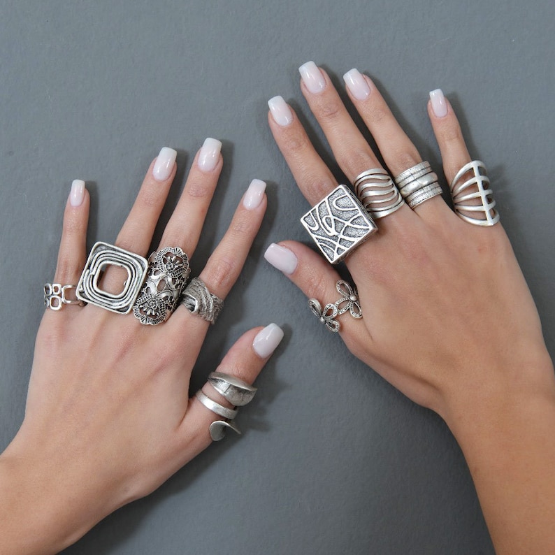 May include: A pair of hands wearing a variety of silver rings. The rings are all different shapes and sizes, and some have intricate designs. The rings are worn on different fingers, and some are stacked on top of each other.