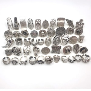 Peut inclure: Une collection de 36 bagues argentées avec différents motifs, y compris des motifs floraux, géométriques et abstraits. Les bagues sont en métal et ont un aspect vintage ou antique.
