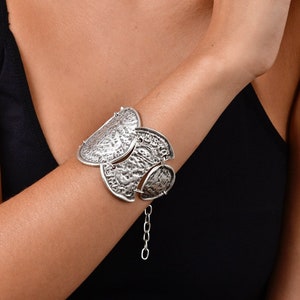 May include: A silver bracelet with a chain and multiple decorative, textured, half-circle shaped charms.