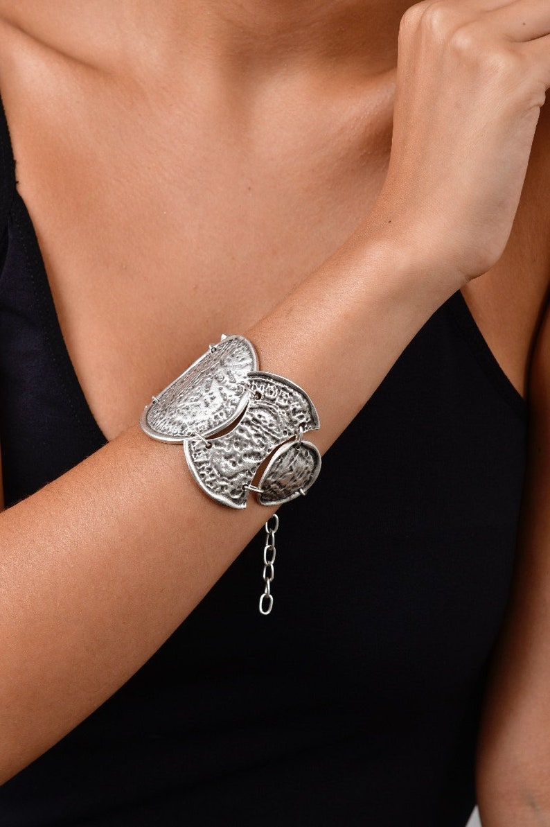 May include: A silver bracelet with a chain and multiple decorative, textured, half-circle shaped charms.