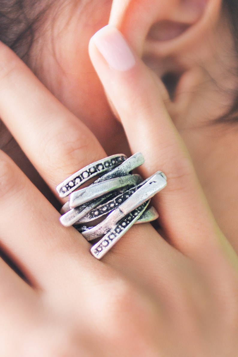 May include: A silver ring with a unique, multi-layered design. The ring is made of several thin bands that are intertwined and decorated with small beads.