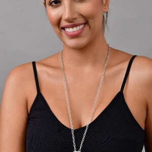 May include: A silver chain necklace with a large, round, textured pendant. The pendant has a detailed design and is hanging on a silver chain.