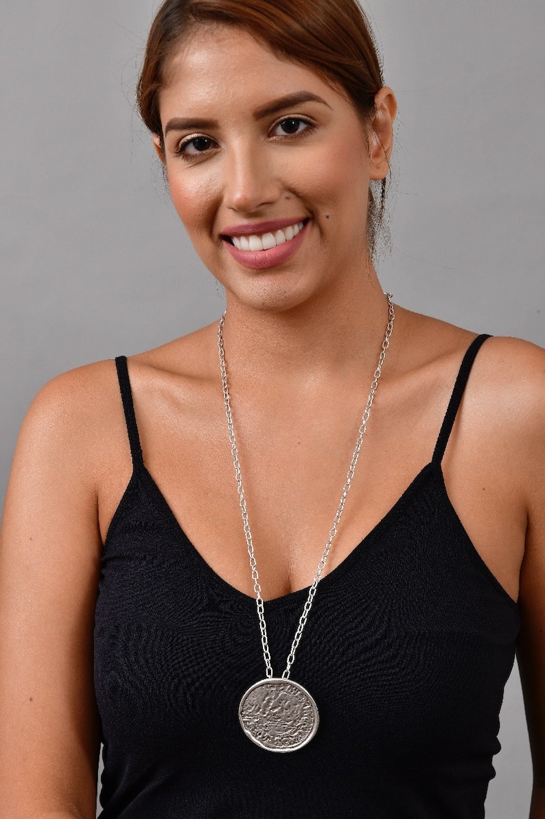 May include: A silver chain necklace with a large, round, textured pendant. The pendant has a detailed design and is hanging on a silver chain.