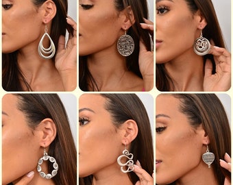 May include: Six pairs of silver dangle earrings with different designs. The earrings are shown on a model's ears.