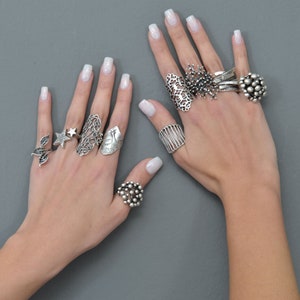 May include: A hand model wearing multiple silver rings with intricate designs. The rings feature a variety of shapes, including stars, leaves, and geometric patterns.