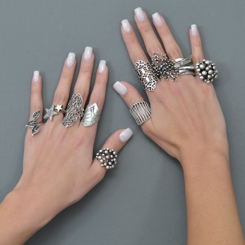 May include: A hand model wearing multiple silver rings with intricate designs. The rings feature a variety of shapes, including stars, leaves, and geometric patterns.