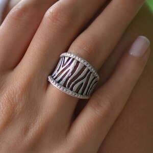 May include: A silver ring with a zebra print design. The ring is wide and has a textured surface.