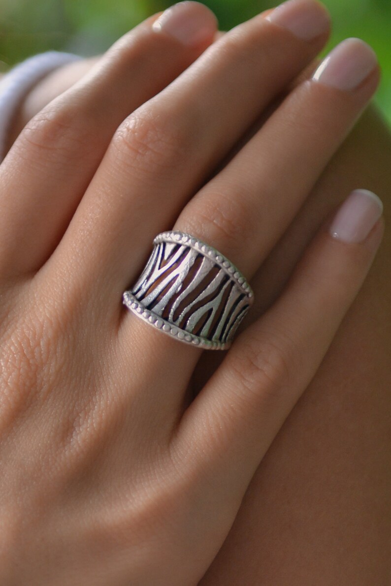May include: A silver ring with a zebra print design. The ring is wide and has a textured surface.