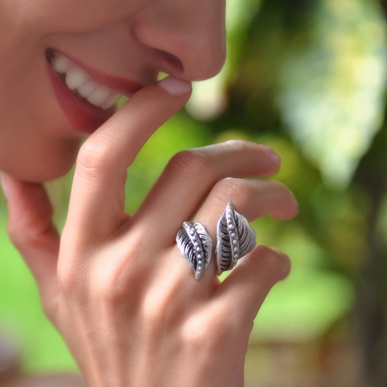 May include: A silver ring featuring two leaf designs. The leaves are textured and have small beads along the edges.