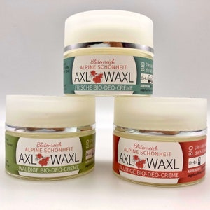 Könnte beinhalten: Drei kleine Gläser mit natürlicher Deocreme mit grünen, roten und weißen Etiketten. Die Etiketten zeigen den Text "Blütenreich Alpine Schönheit AXL WAXL" und die Worte "Frische Bio-Deo-Creme", "Waldige Bio-Deo-Creme" und "Blumige Bio-Deo-Creme".