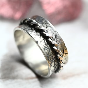 May include: A silver ring with a textured band and a twisted silver wire design. The ring is a wide band and has a hammered finish.