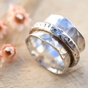 May include: A silver spinning ring with a hammered finish. The ring has a band that spins freely around a central band. The central band has a textured design.