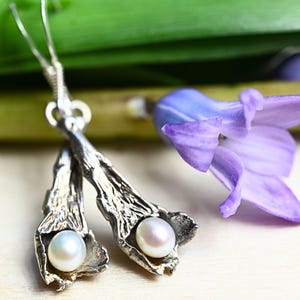 May include: Silver earrings with a textured, organic design. Each earring features a small, white pearl nestled in a delicate, leaf-like shape.