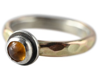 May include: A silver ring with a hammered gold band and a round amber gemstone set in a silver bezel.