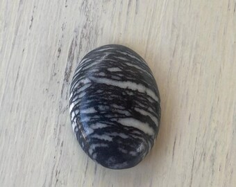 May include: A smooth, round, black and white striped stone. The stone has a natural, polished finish.