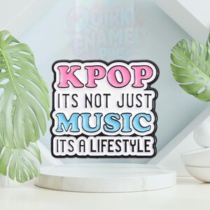 以下が含まれることがあります： 「KPOP ITS NOT JUST MUSIC ITS A LIFESTYLE」のテキストが入った長方形のエナメルピン。ピンは黒い縁取りで、「KPOP」はピンク、「MUSIC」は青、残りは白で書かれています。